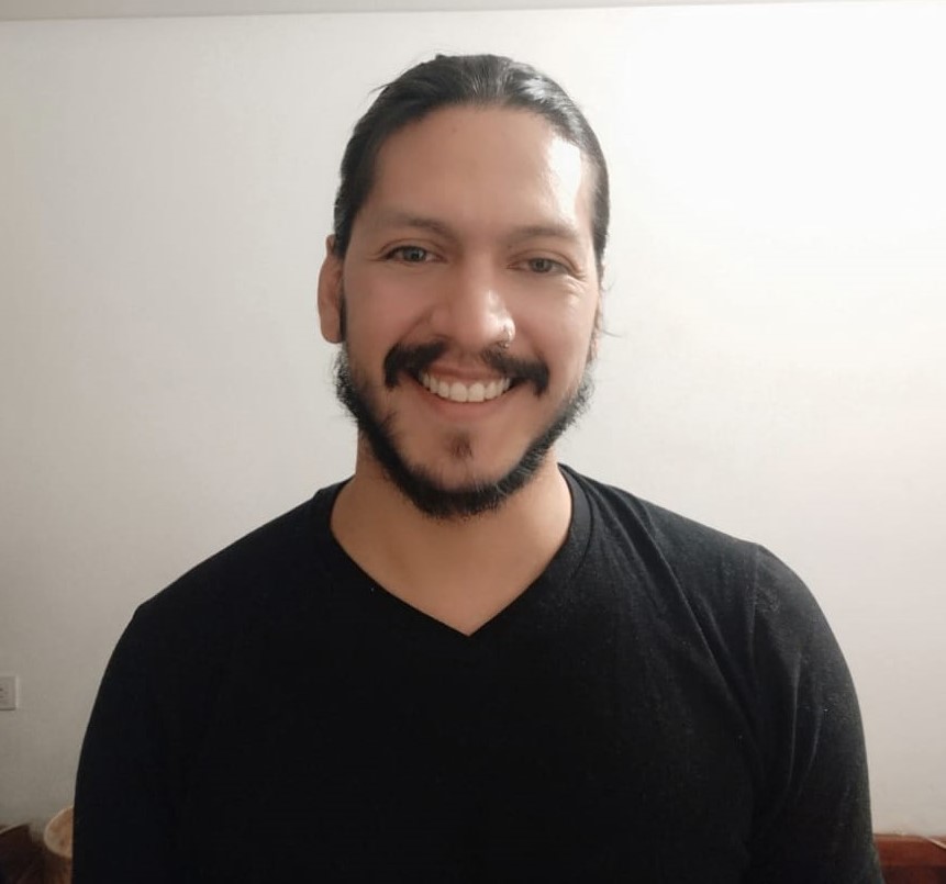 hombre joven, cabello y barba oscuros, sonriendo.